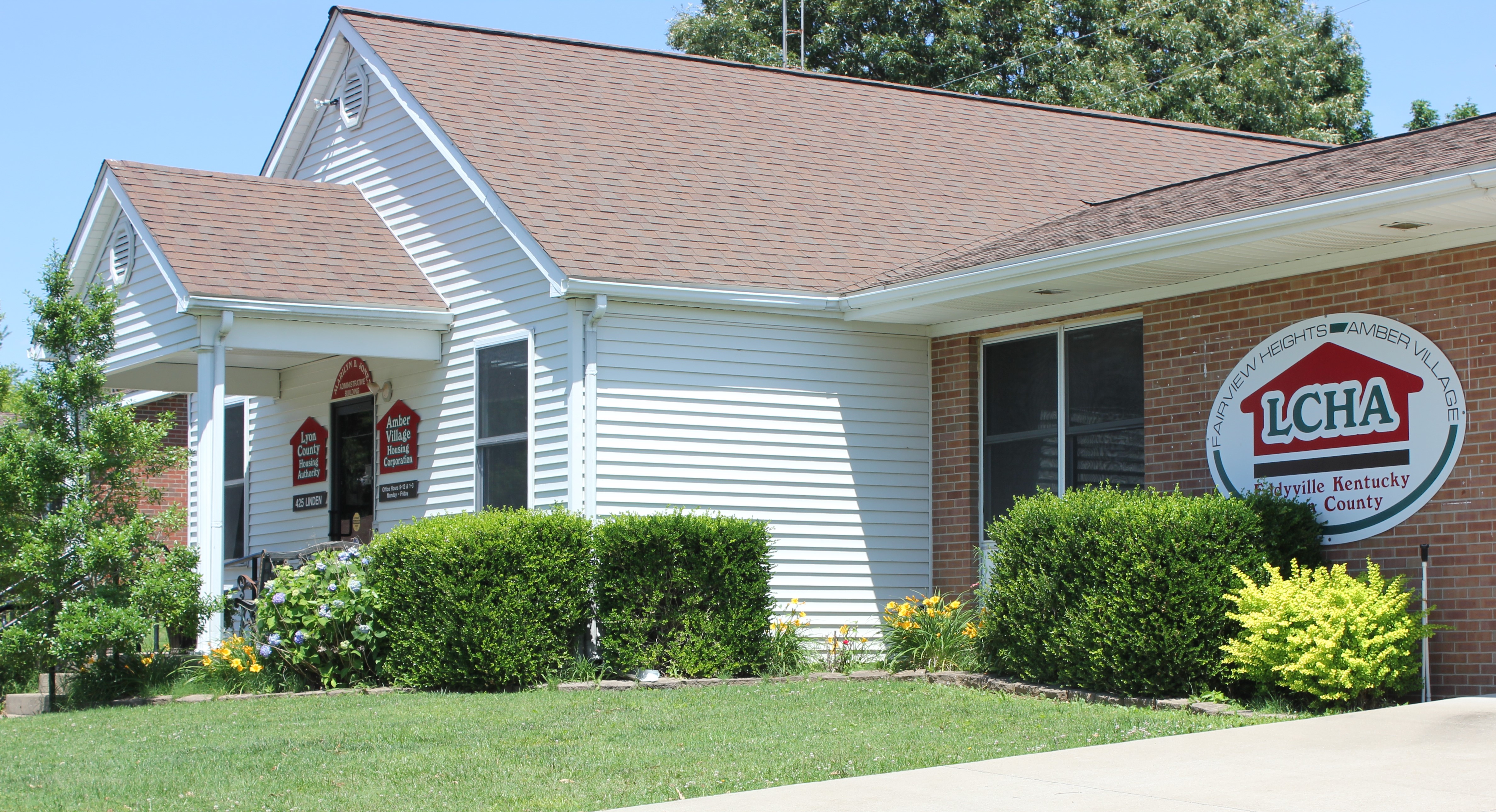 This shows an image of a building with white sides, out front are bushes and a neatly kept lawn, on the front is a sign that reads lyon county housing authority